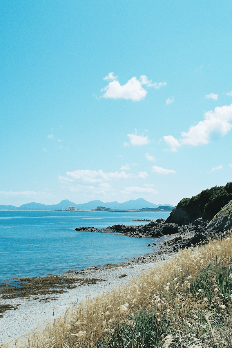 A serene coastal landscape featuring a rugged rocky shoreline and gentle waves under a clear blue sky, with distant mountains visible on the horizon.