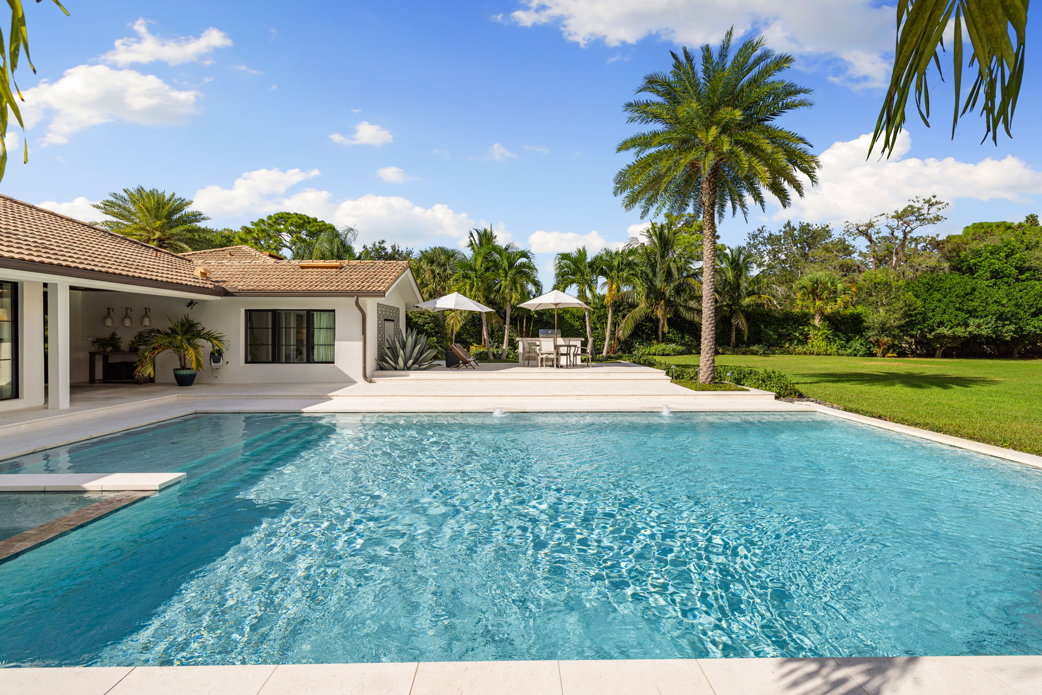 a large square pool next to a modern, villa styled home