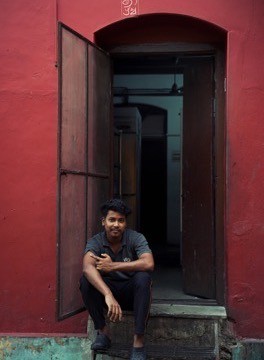 A man seated in a red painted doorway in Fort Kochi