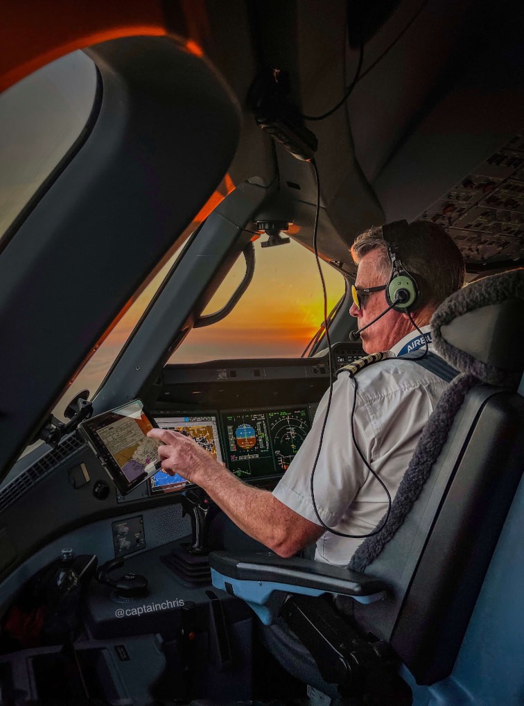 Captain Chris flying an aircraft at sunset inside the cockpit while monitoring navigation instruments.