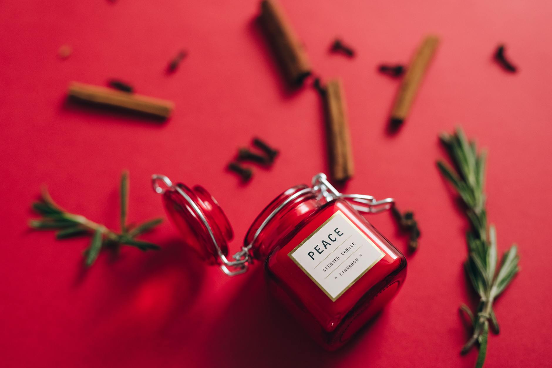 Close-up of a red scented candle with rosemary and cinnamon on a red background.