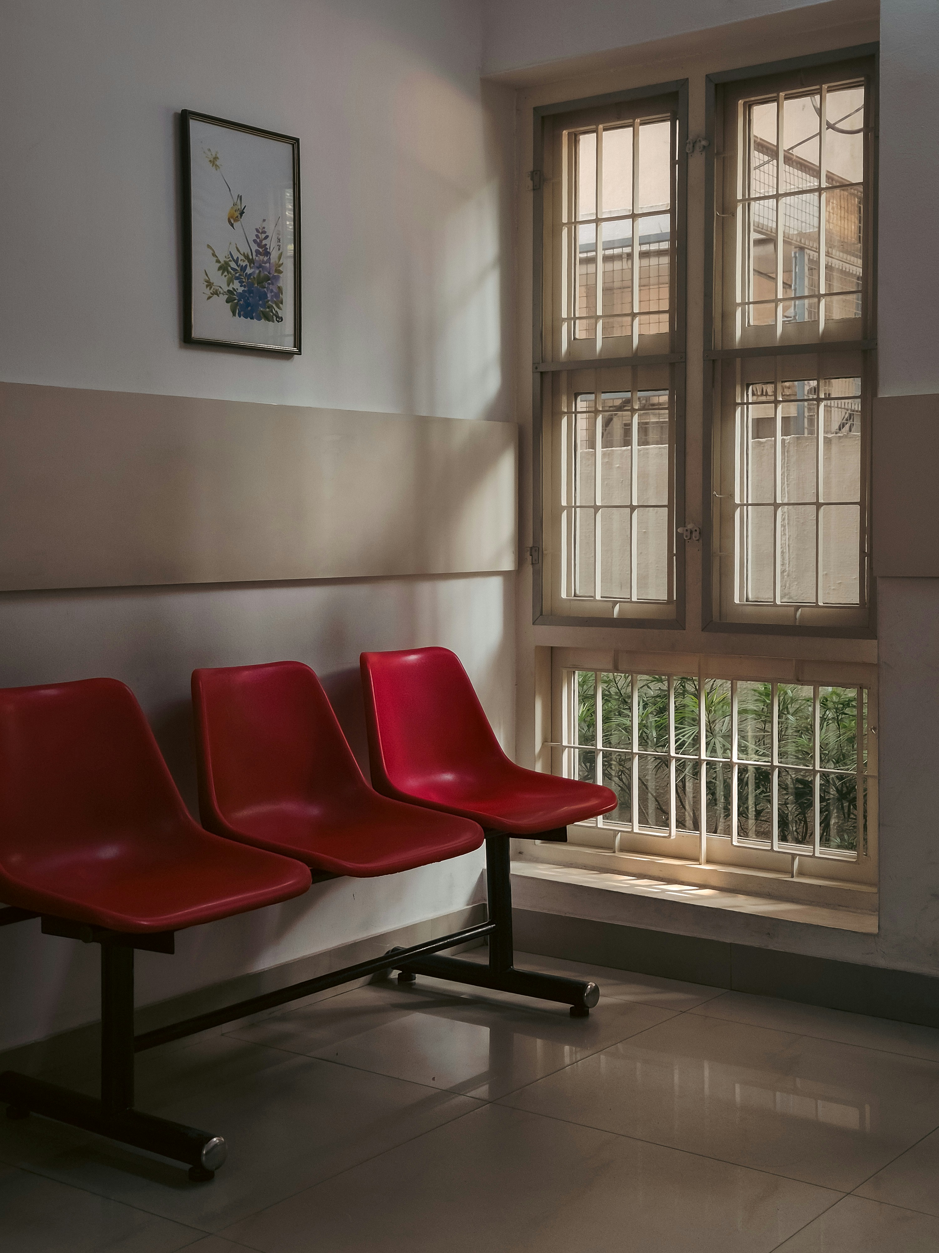 Three red chairs in a waiting room by window