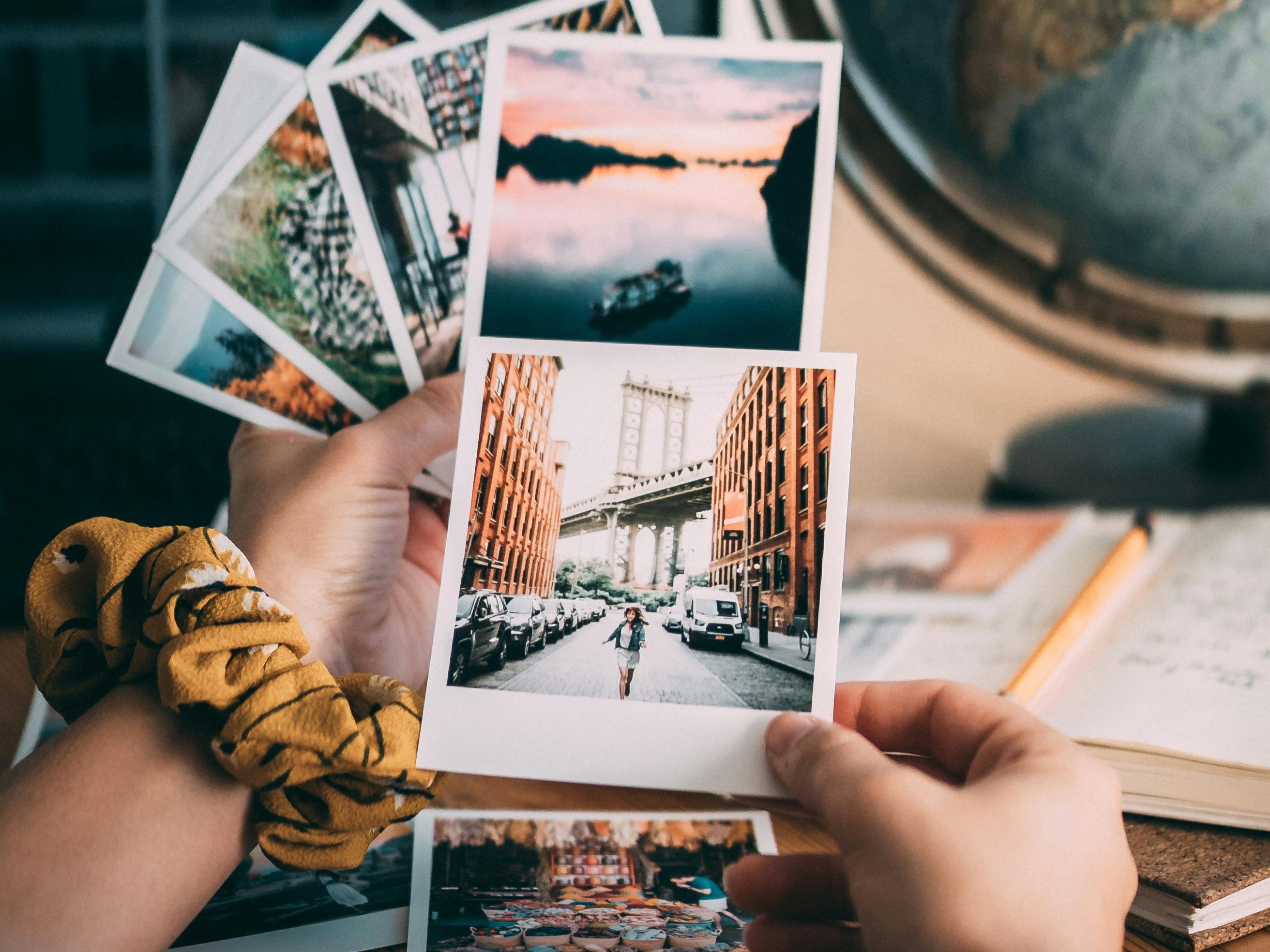 A person holding a collection of colorful travel photos, with a globe and journal in the background, evokes themes of exploration, wanderlust, and cherished memories. This image highlights the joy of documenting and reminiscing about adventures.