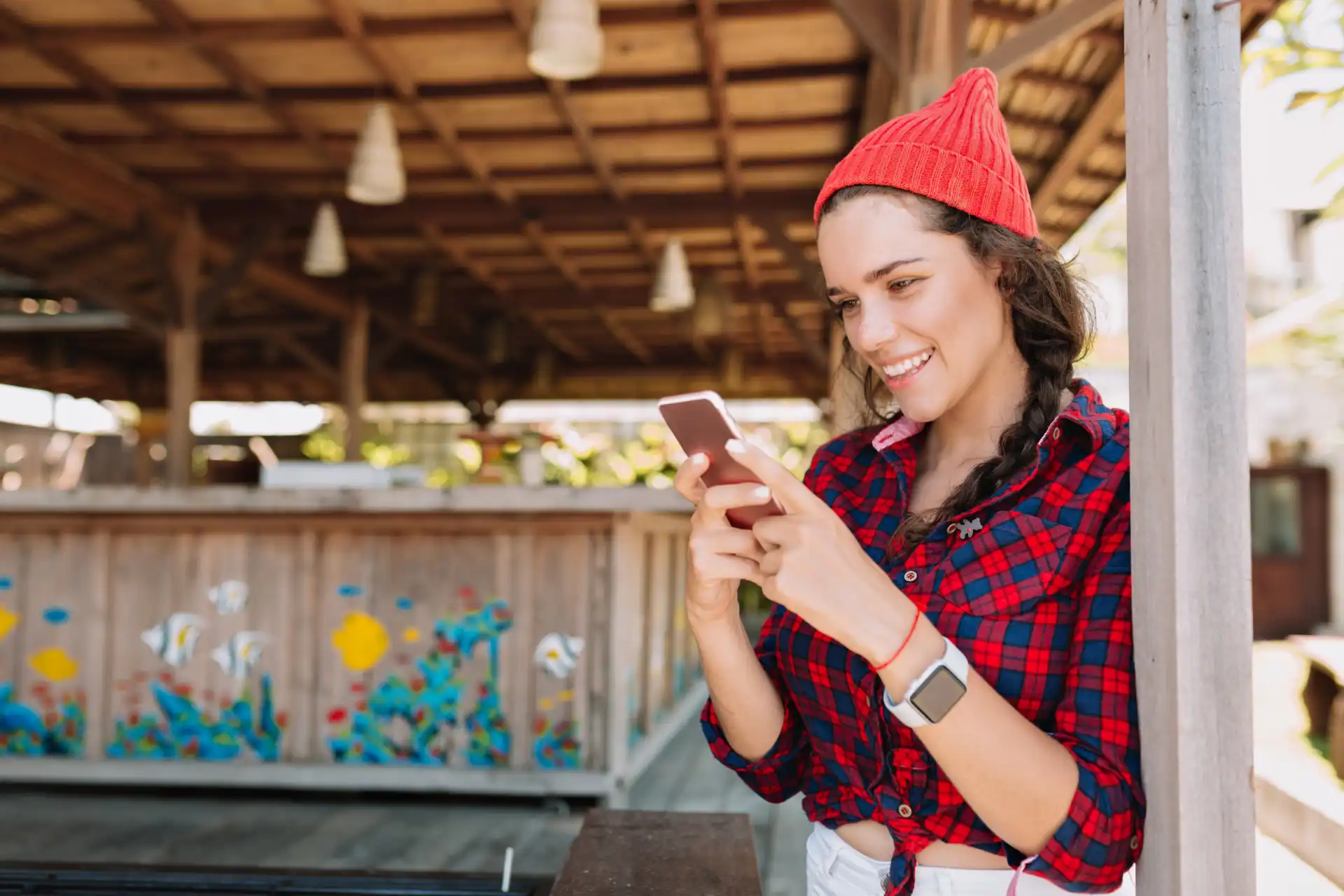 Smiling Gen Z woman in red beanie scrolling through TikTok Shop feed on smartphone outdoors.