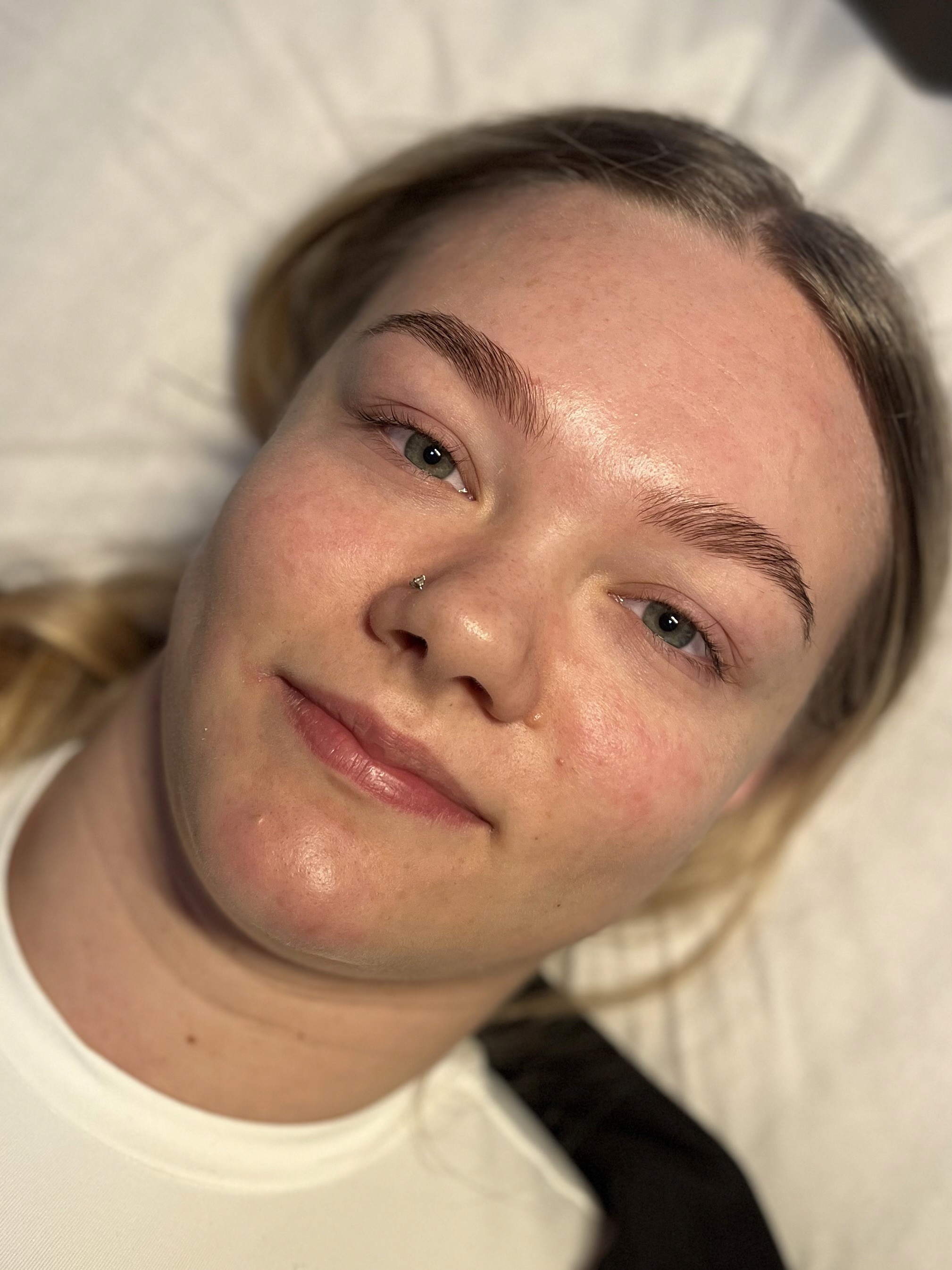 A woman with a serene expression lies on a white pillow. She has neatly shaped eyebrows and fair skin. Her gaze is calm and relaxed.