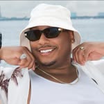 A young man with light brown hair is wearing a black suit jacket and white shirt, standing in a softly lit office setting, conveying professionalism.