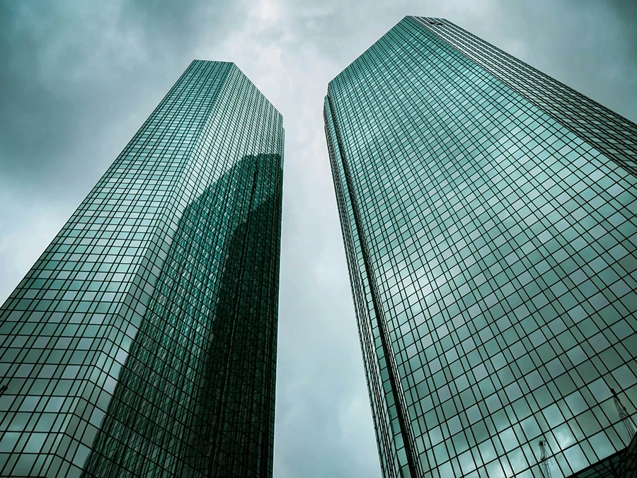 Photo of two skyscrapers with glass facades against a clouded sky.