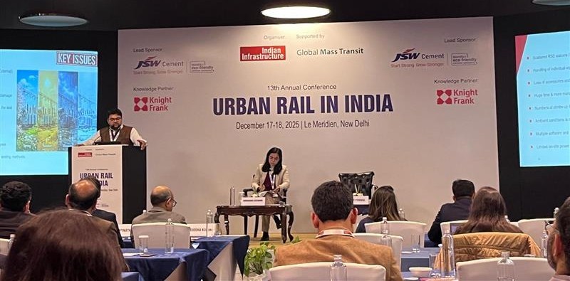 A man stands while two people sit at a table in an office setting, smiling and engaged in conversation. The mood is friendly and collaborative.