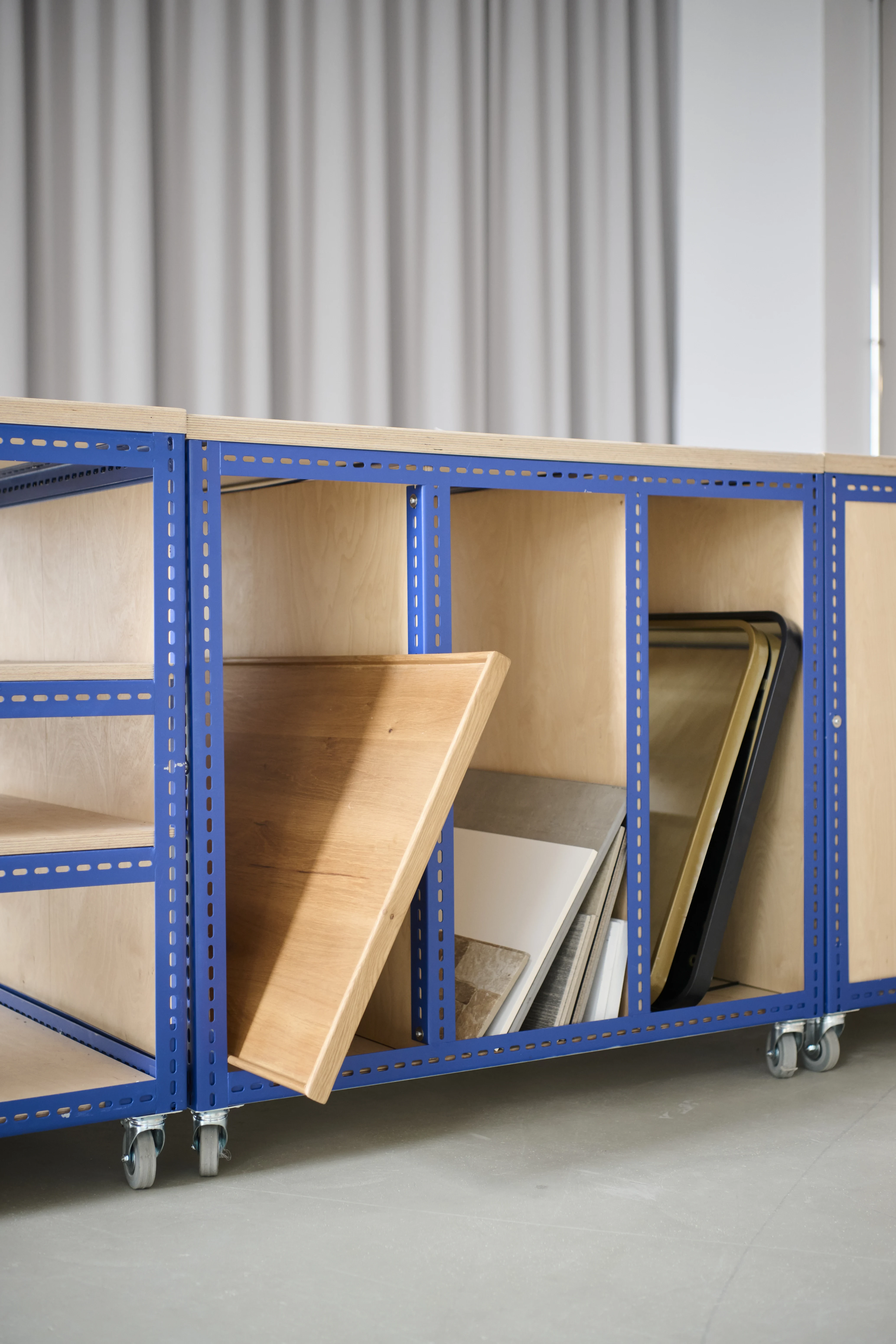 Detail of the blue steel-framed plywood storage module at the FLACONI CONTENT STUDIO with compartments for boards and trays on lockable castors.