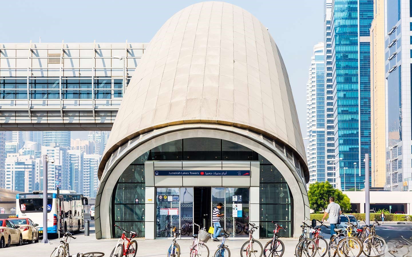 Entrance of Jumeirah Lakes Towers Metro Station with its dome-shaped structure, bicycles outside, and tall skyscrapers behind.