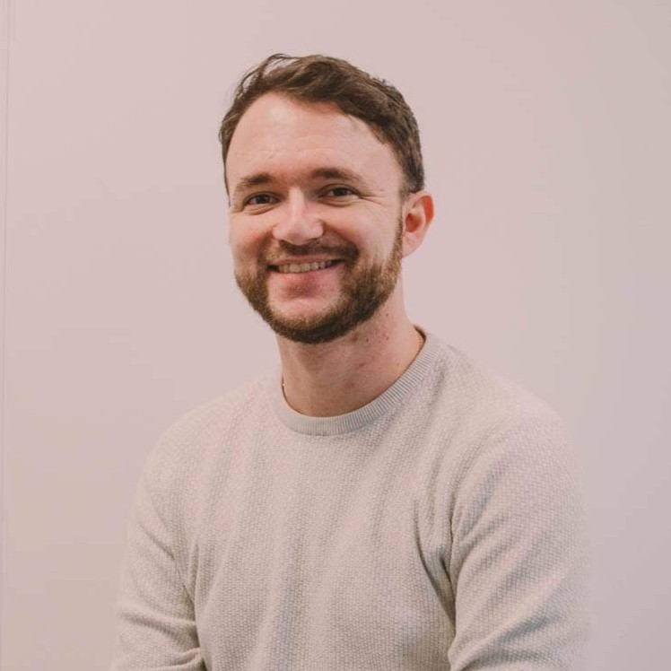 A photo of me, facing the camera, smiling, wearing a jumper, with a neutral coloured background