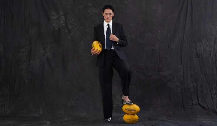 Female athlete posing in a tailored black suit with footballs