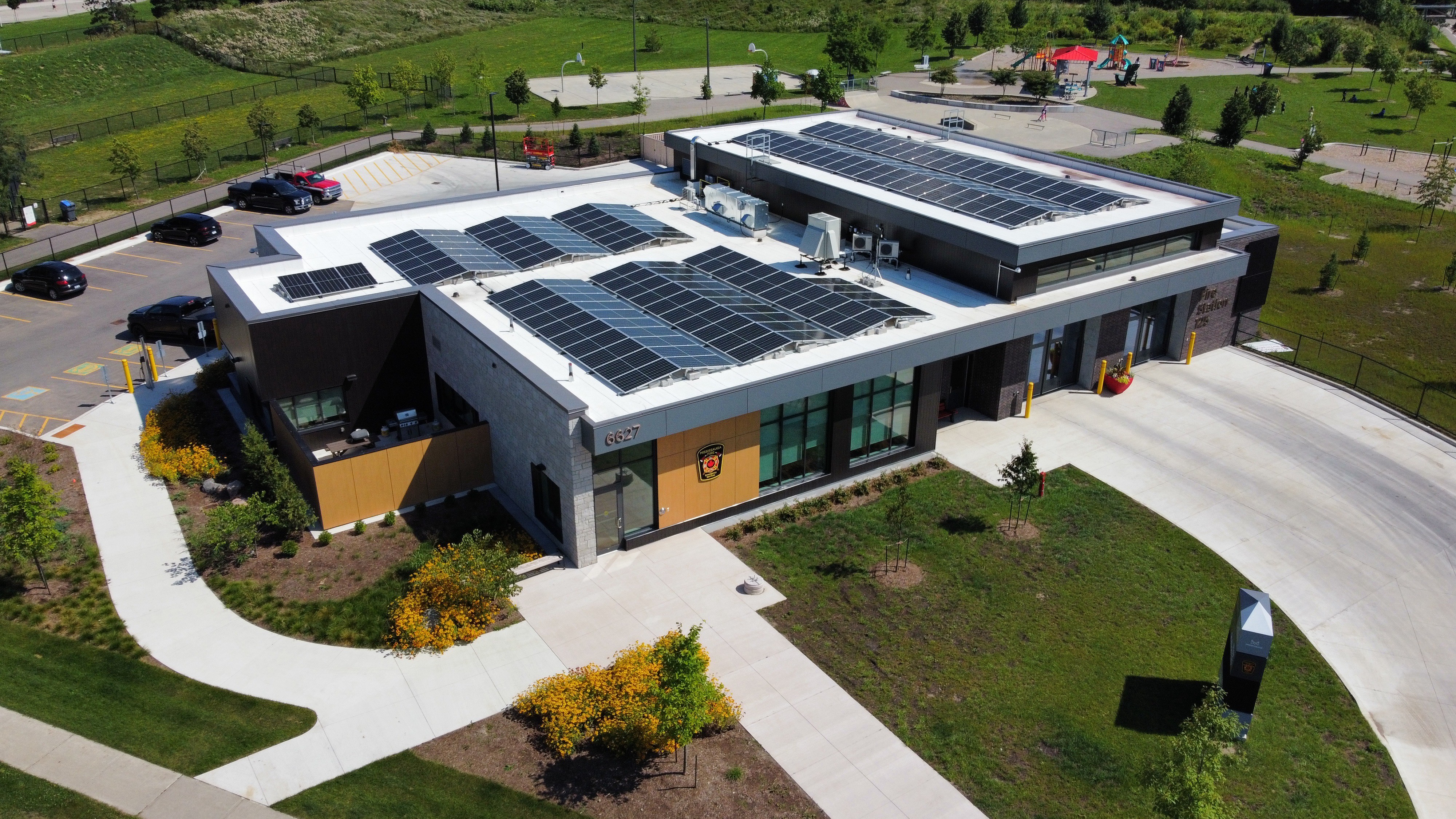 Modern building with solar panels, surrounded by greenery and a curved pathway. Aerial view.