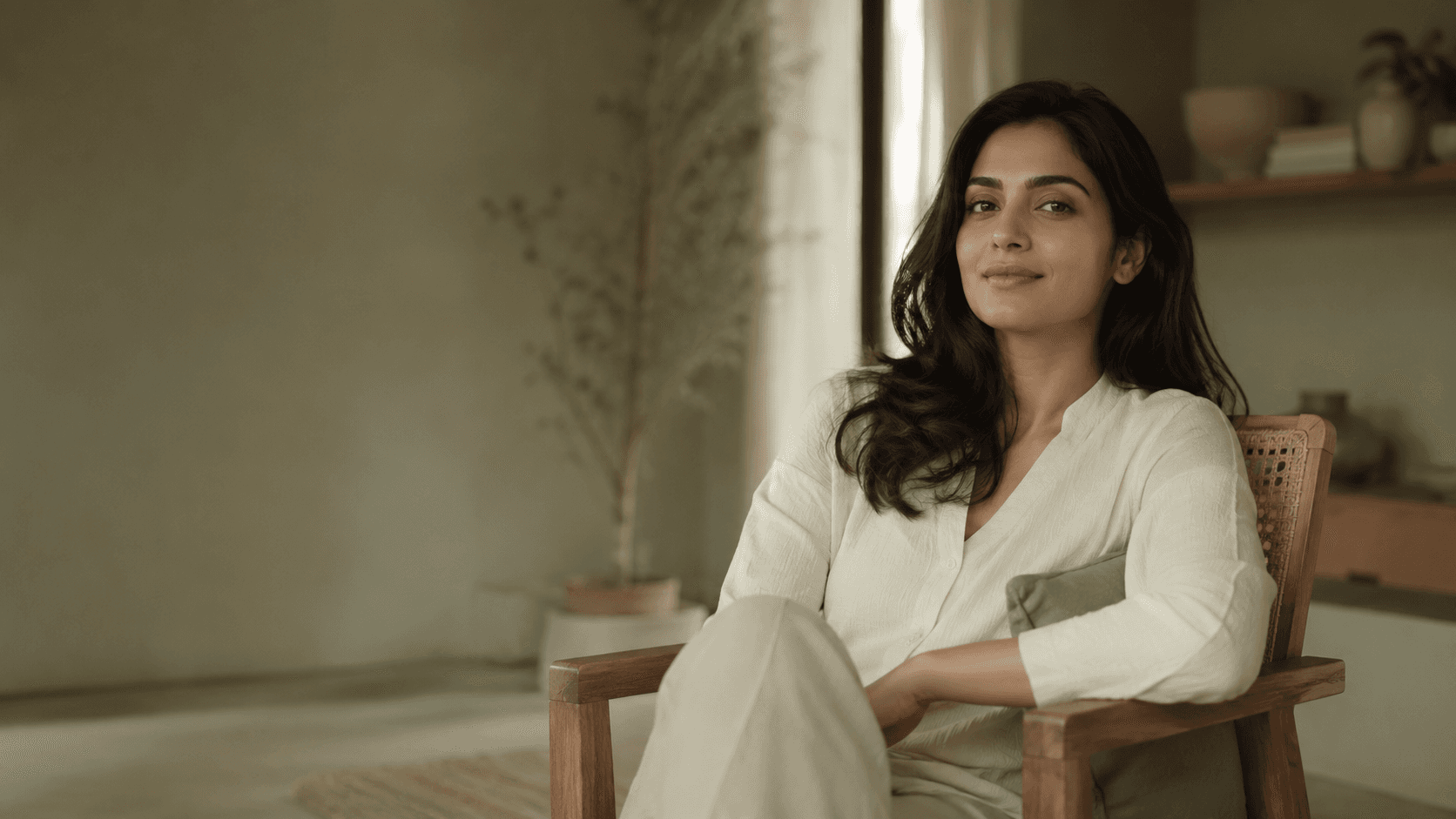 A woman relaxing in a wooden chair by a window in a calm, softly lit room