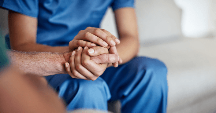 Care worker holding a patient’s hands in a supportive gesture.