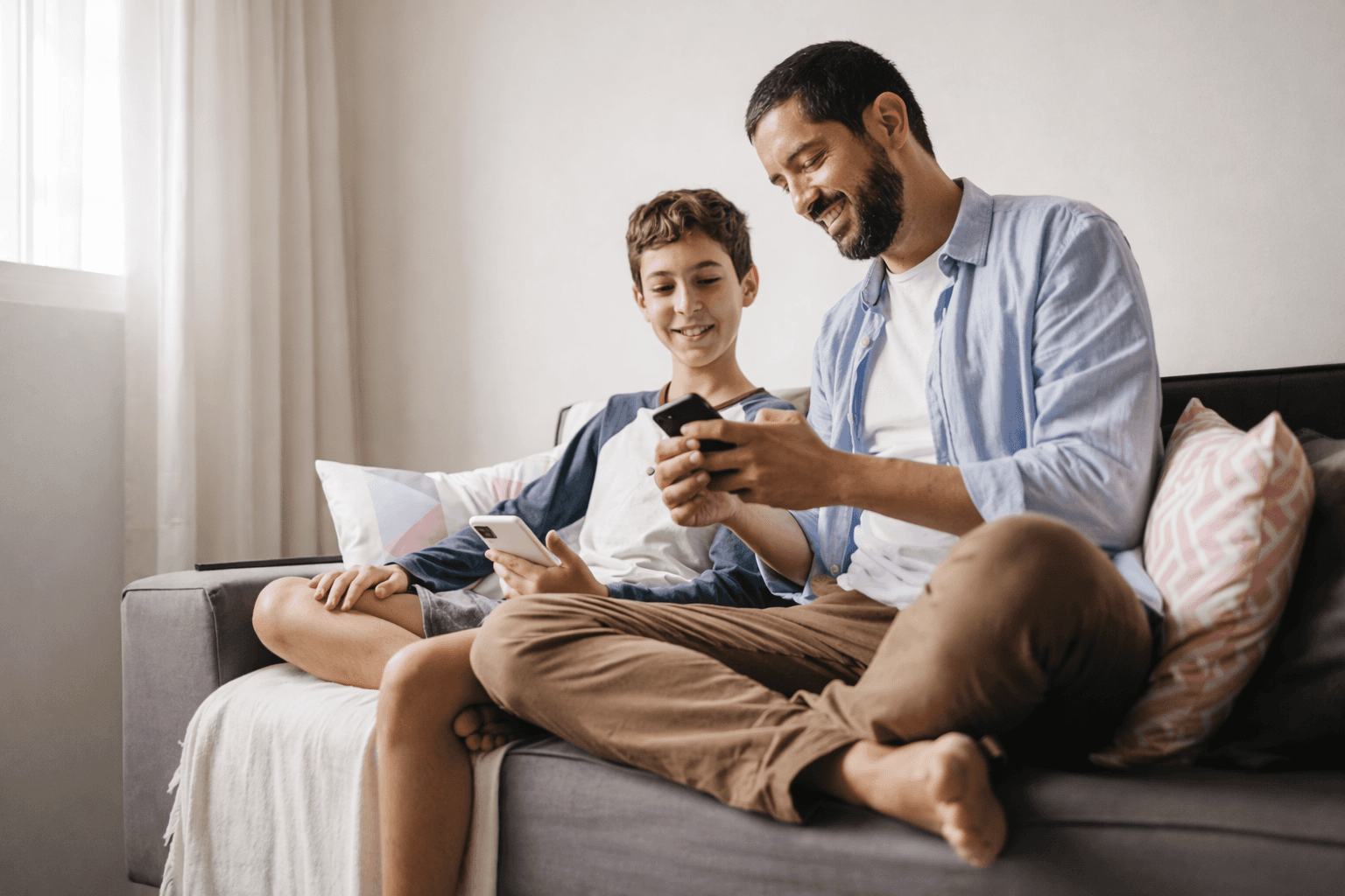 Parent and teenage child sitting on a couch and looking at smartphones together.