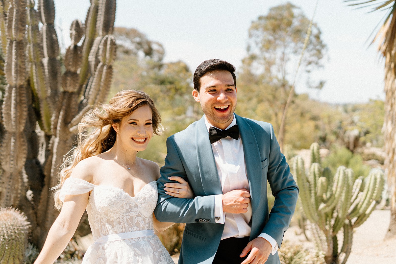 A San Diego couple in formal attire walks together in nature, smiling and enjoying a moment outdoors.