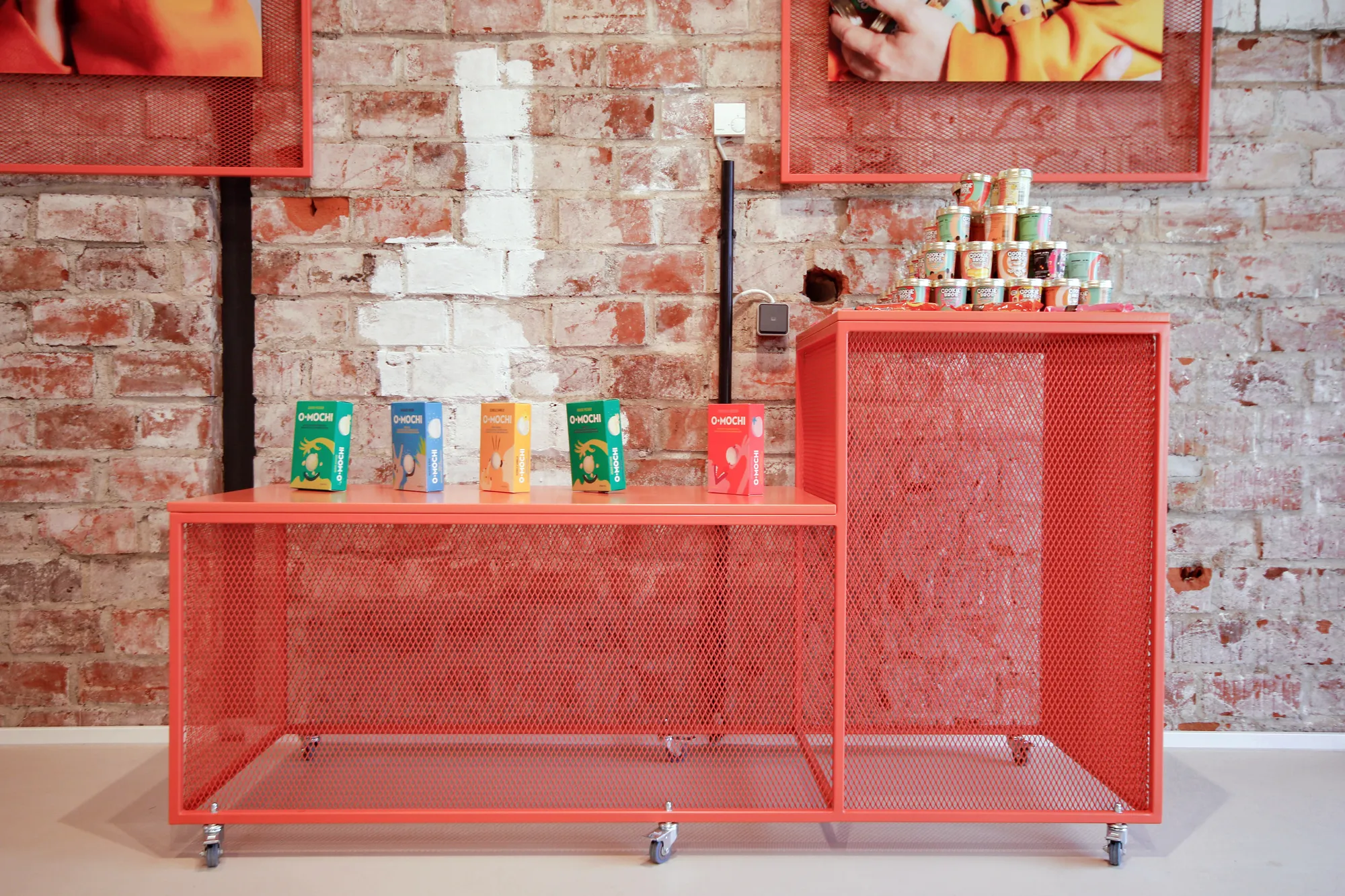 Red mesh display tables with packaged products against the brick wall.