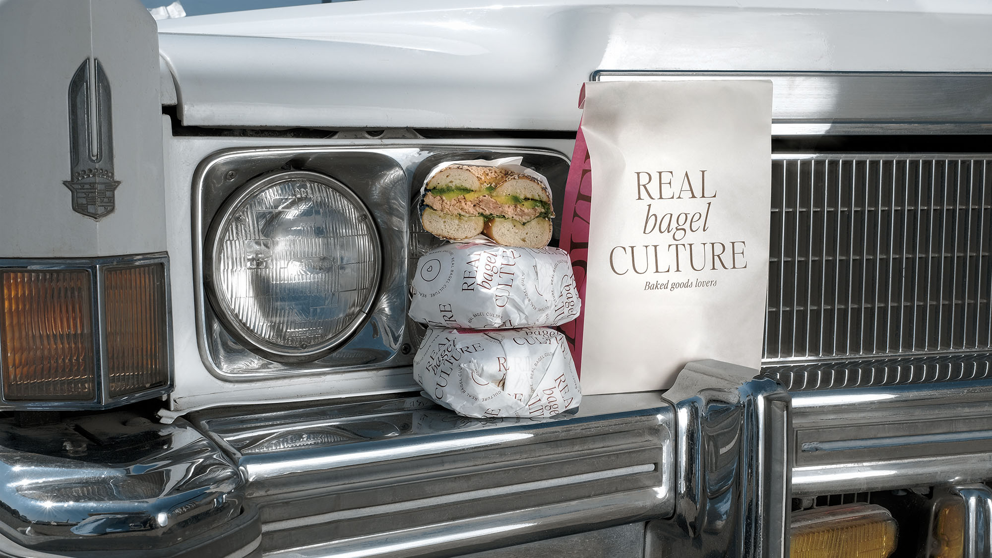Bagels on a car with "Real Bagel Culture" bag. Two wrapped bagels stacked with one open bagel sandwich.