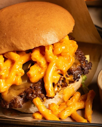 A delicious cheeseburger topped with macaroni and cheese and crispy cheese curls, served in a paper wrapper.