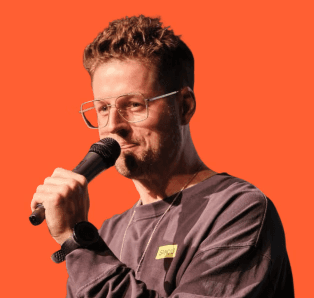 Smiling young man with short hair poses against a dark background, wearing a green button-up shirt.