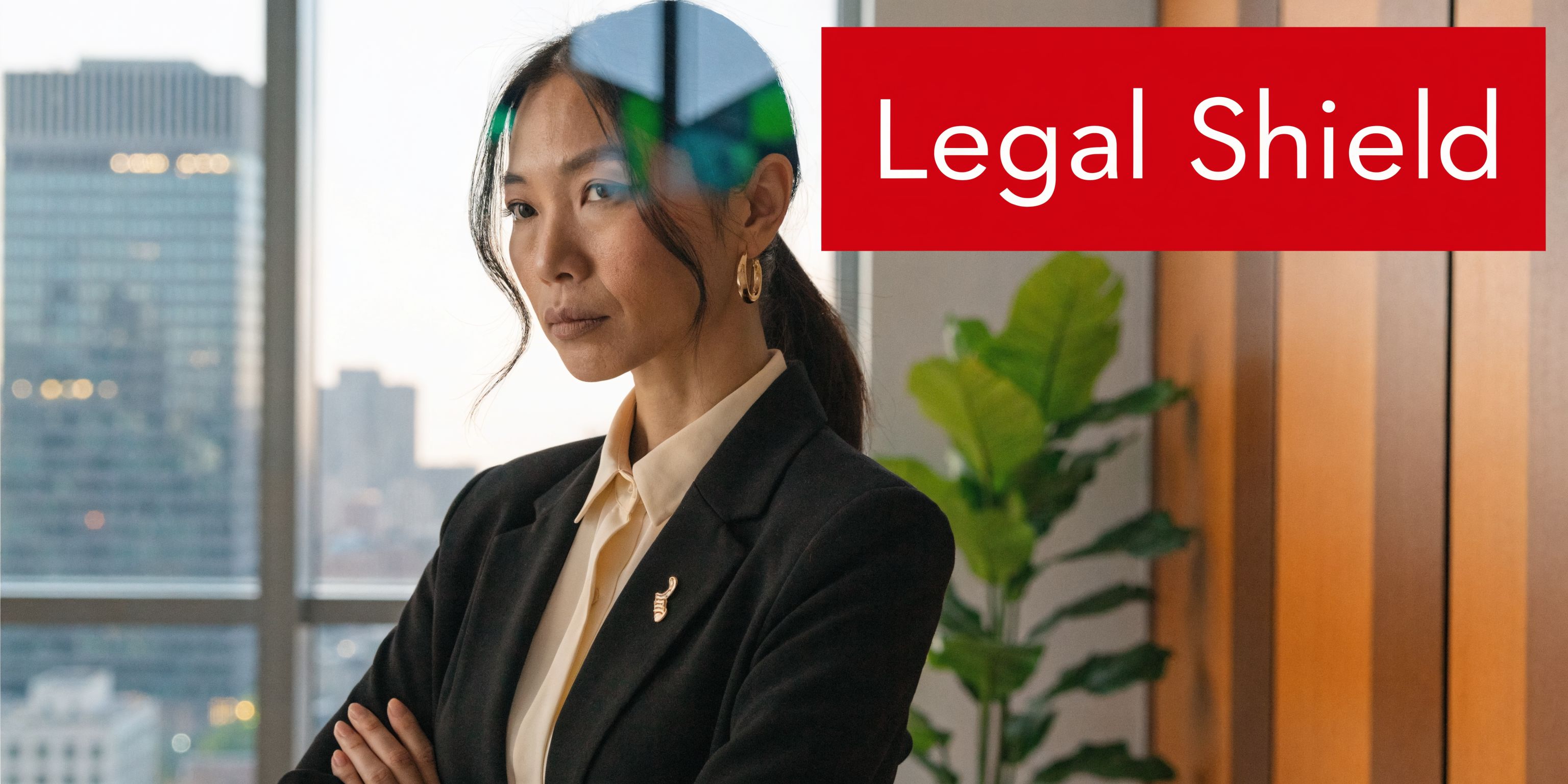 A professional woman in a business suit standing in front of an office window looking serious.