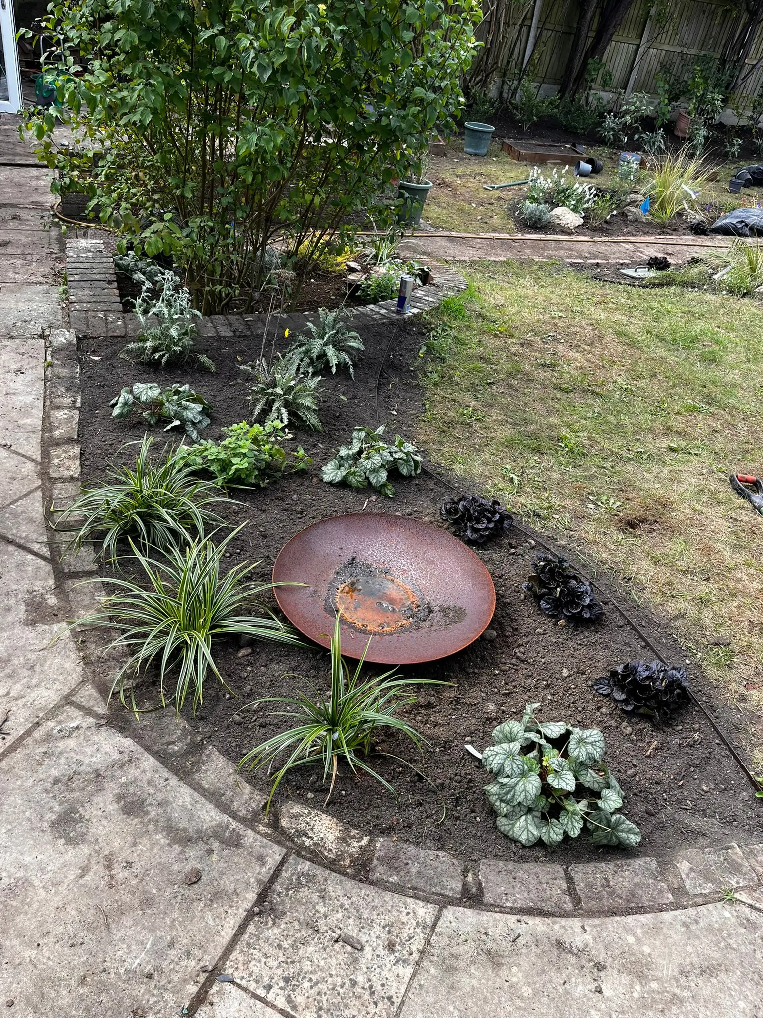 A garden area featuring a round stone, surrounded by various plants and a stone path.