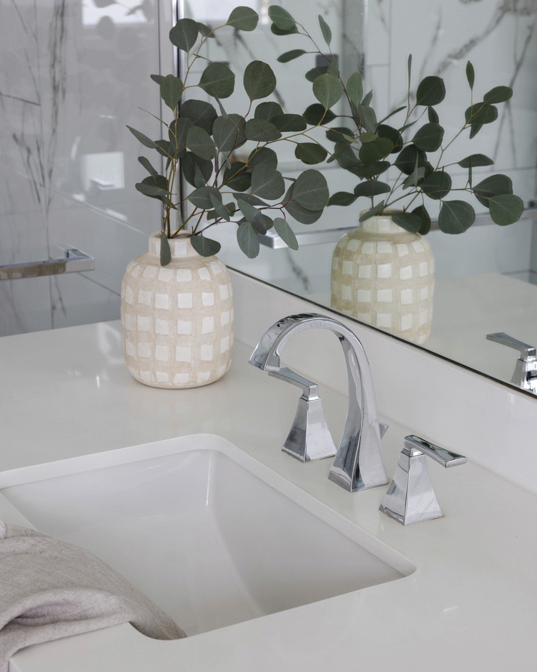 Close up of vanity sink with chrome faucet and ceramic vase with greenery