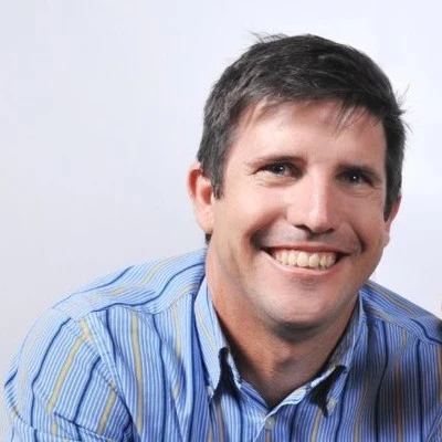 Man in denim jacket smiling outdoors.