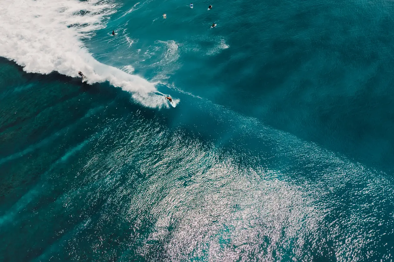 Aerial view of a surfer riding a turquoise ocean wave, illustrating the metaphor of resilience as the buffer for life's inevitable waves
