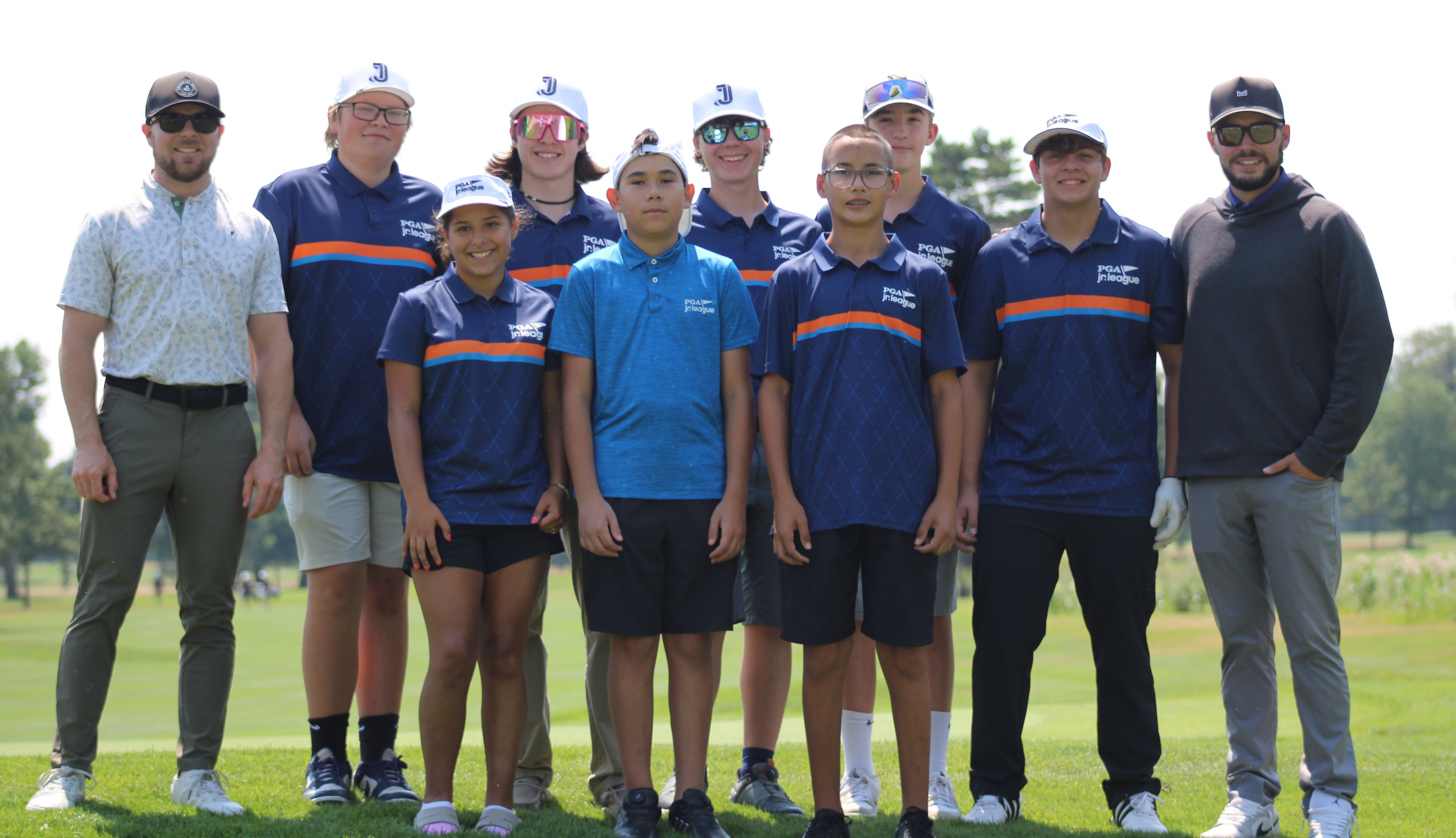 A group of students at the edge of a green, chipping balls towards net targets.