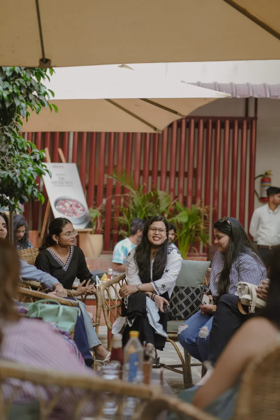 A group of people gathered outdoors, sitting around a table under umbrellas, engaged in conversation.