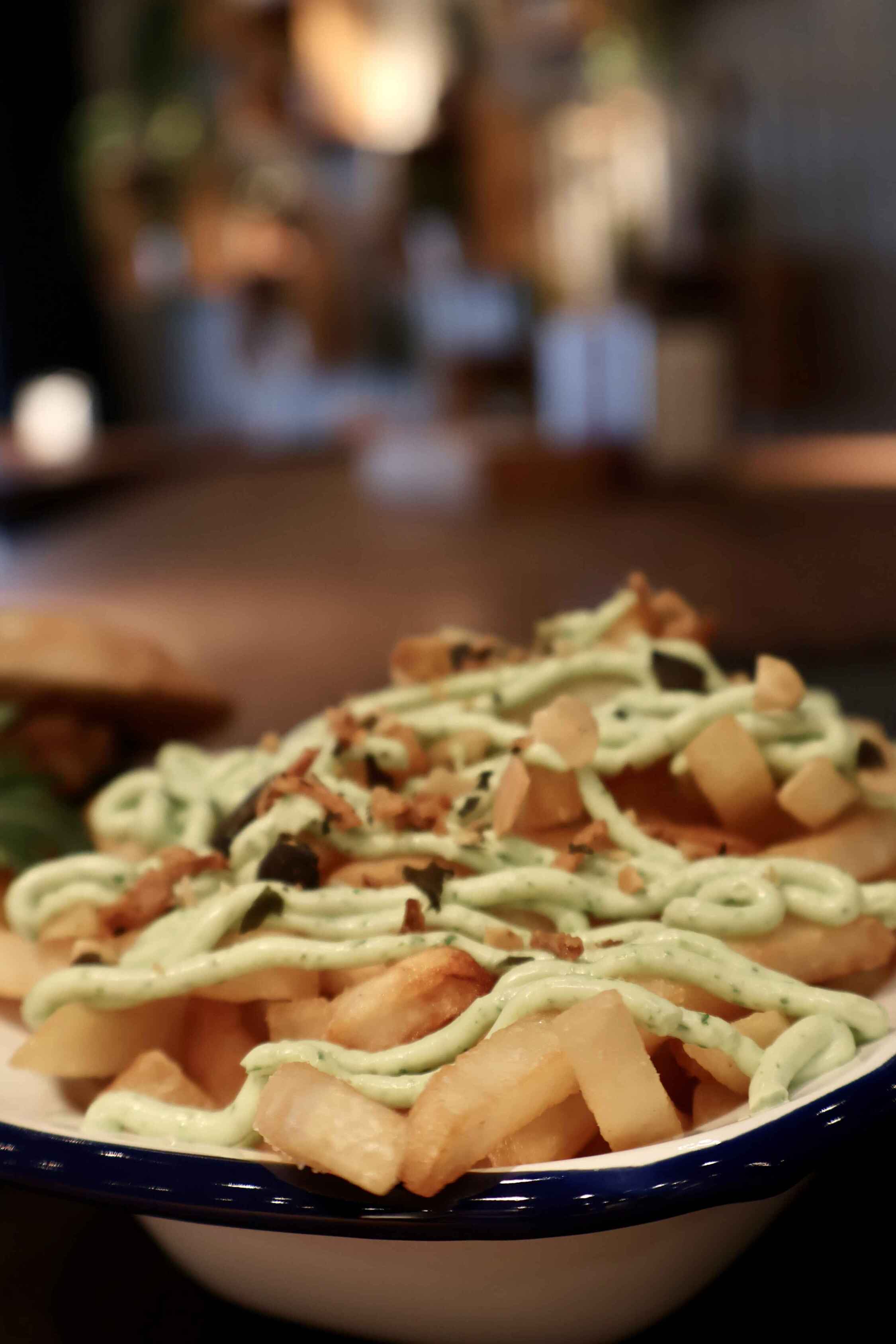 Overhead view of a kAlps Foodbar table spread with burgers, crispy fries, fondue dishes, a red cocktail, dipping sauces, and fresh garnishes arranged on slate serving boards.
