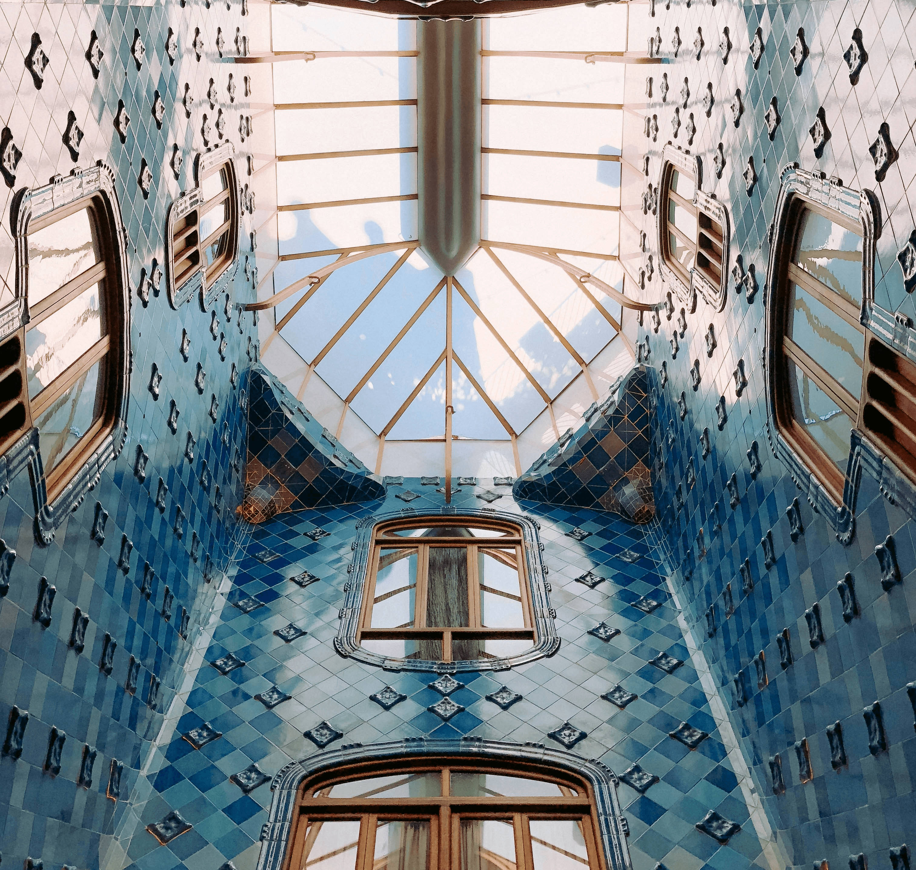 Light pours through a skylight into an airy atrium lined with blue tiles and windows in Casa Batllo.