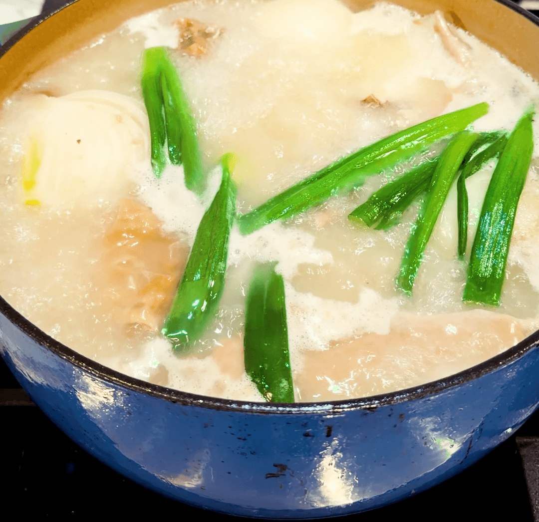 a pot of boiling broth with green onions on the top