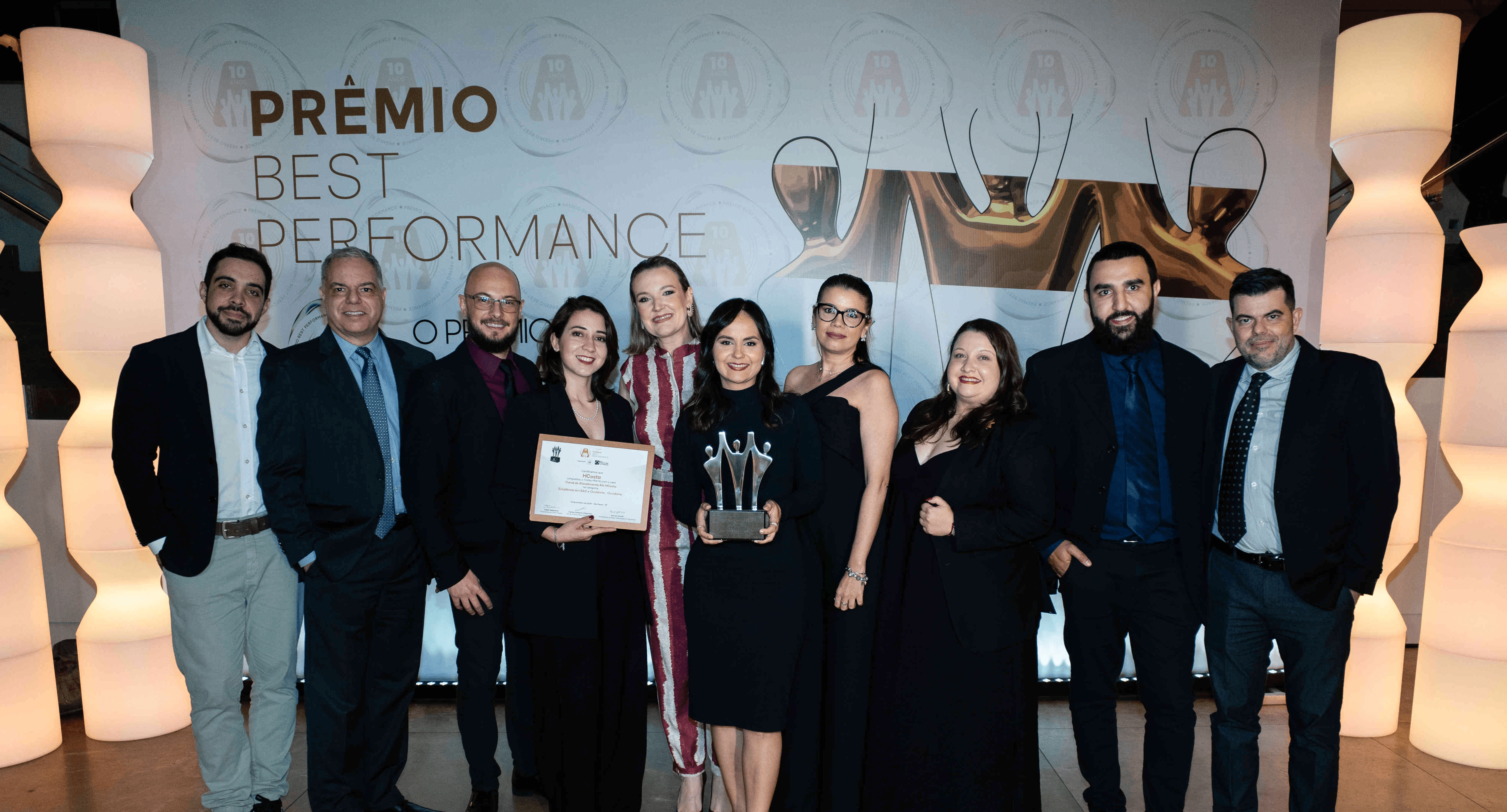 Executivos da HCosta posando com troféu prata e certificado no palco do Prêmio Best Performance 2025