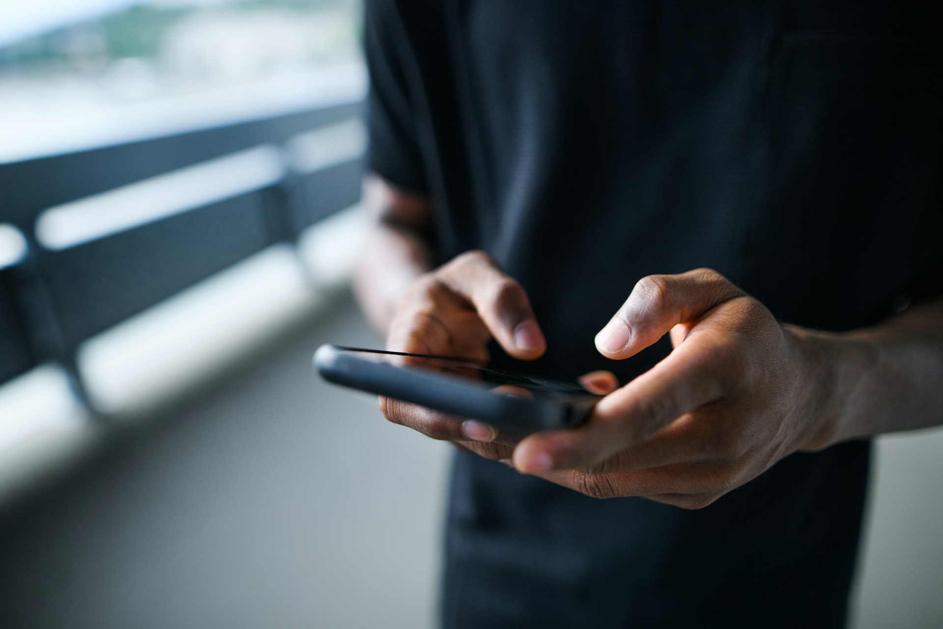 Close-up of a person’s hands holding a smartphone, tapping the screen while standing outdoors.