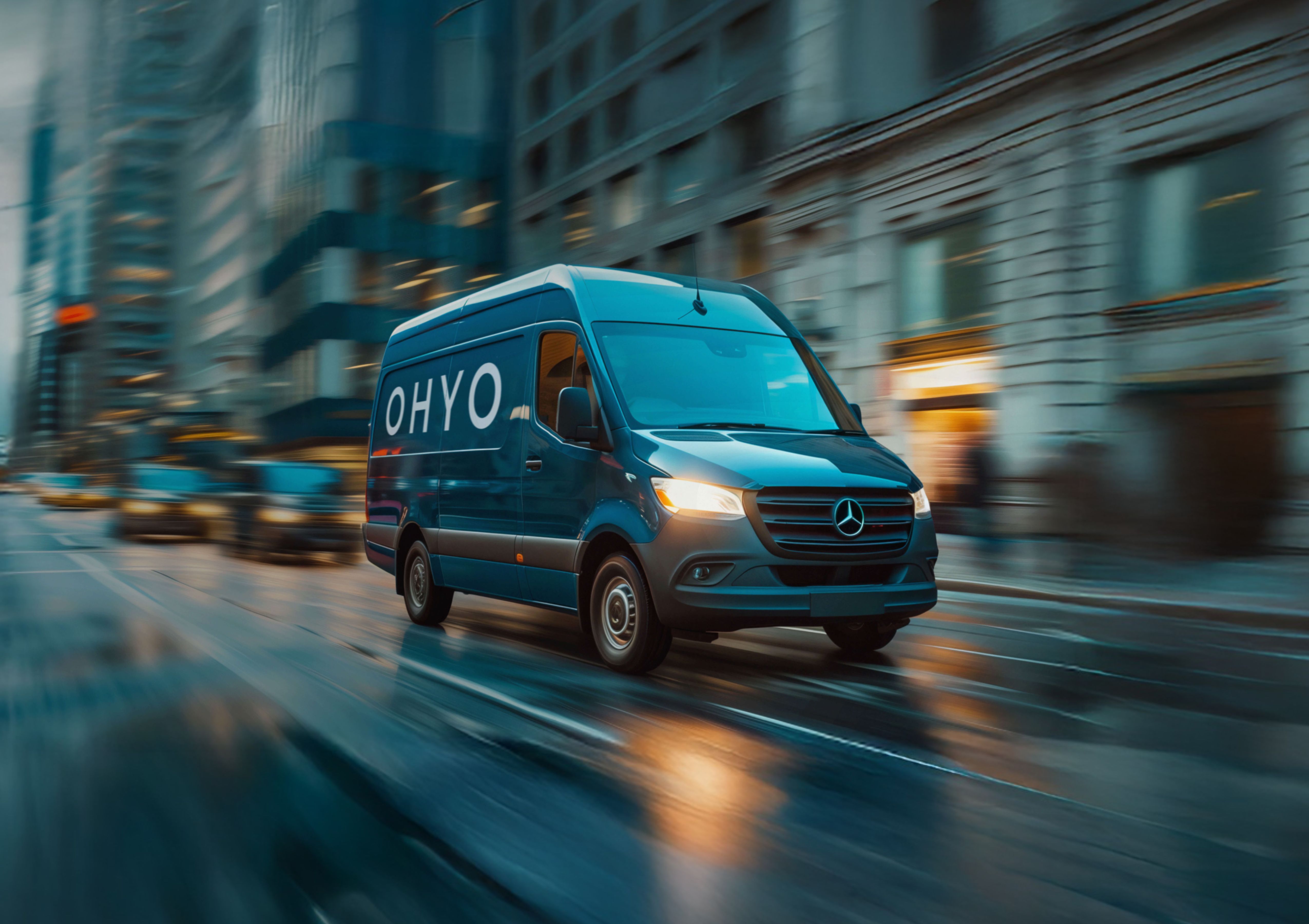 Blue Mercedes-Benz van with OHYO branding driving through a city street on a rainy day, conveying motion and speed.