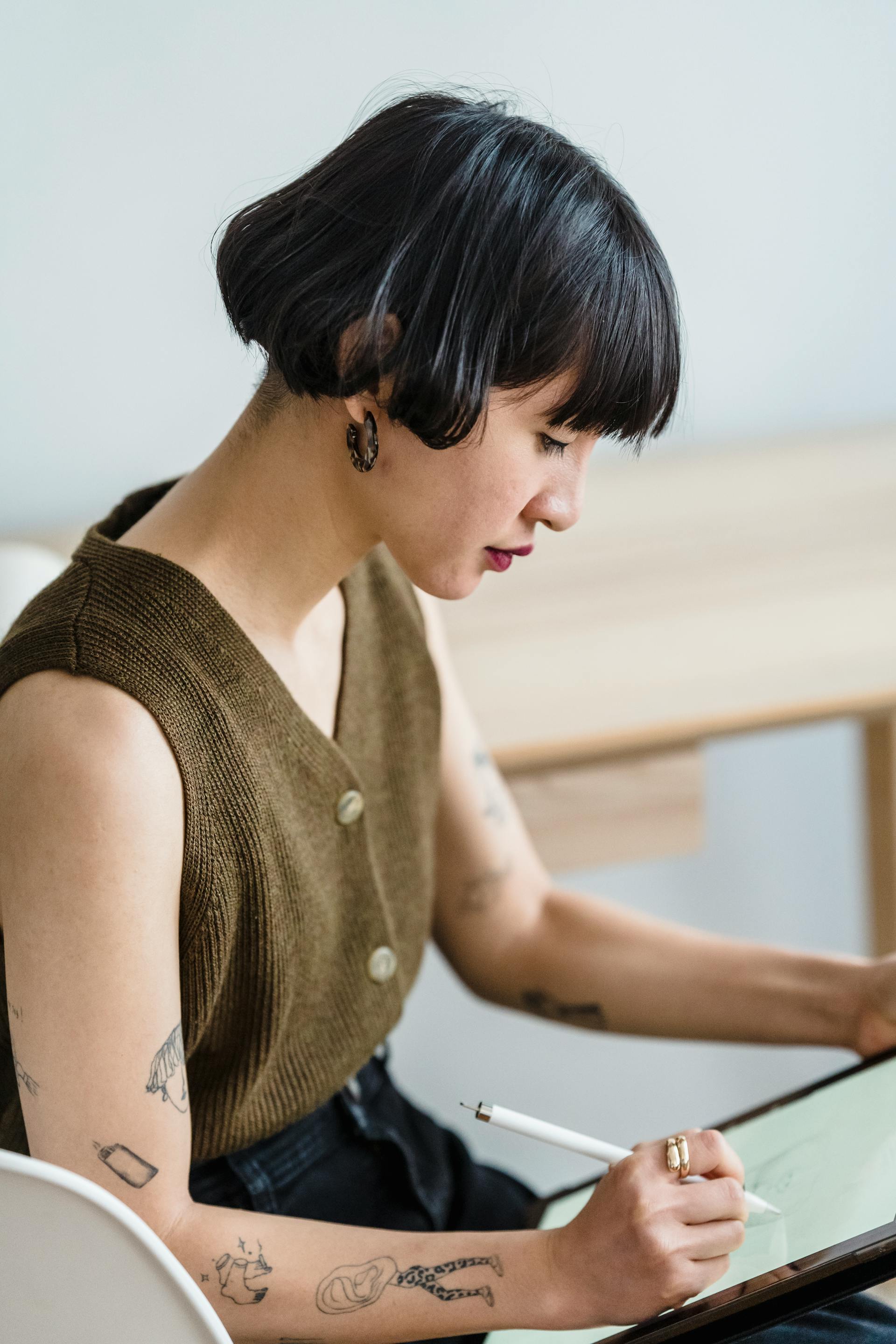 A side view of a woman with purffed short hair focusing on drawing on an ipad
