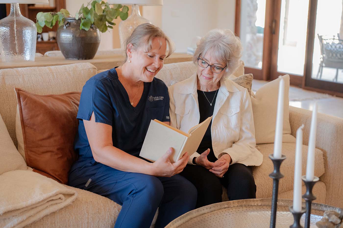 Two women sitting on a couch looking at a book.