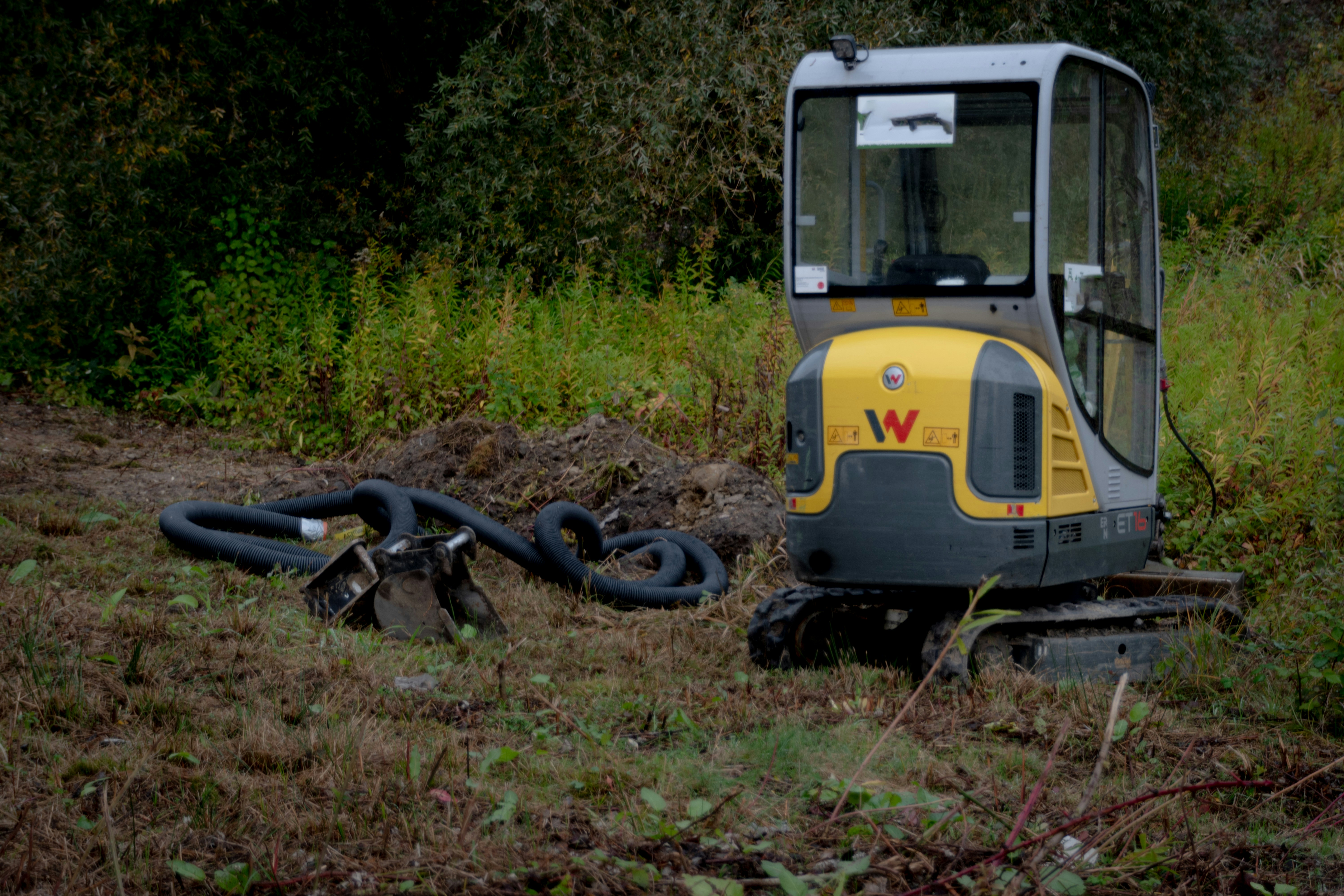 Mini excavator parked on grassy terrain with hoses nearby.