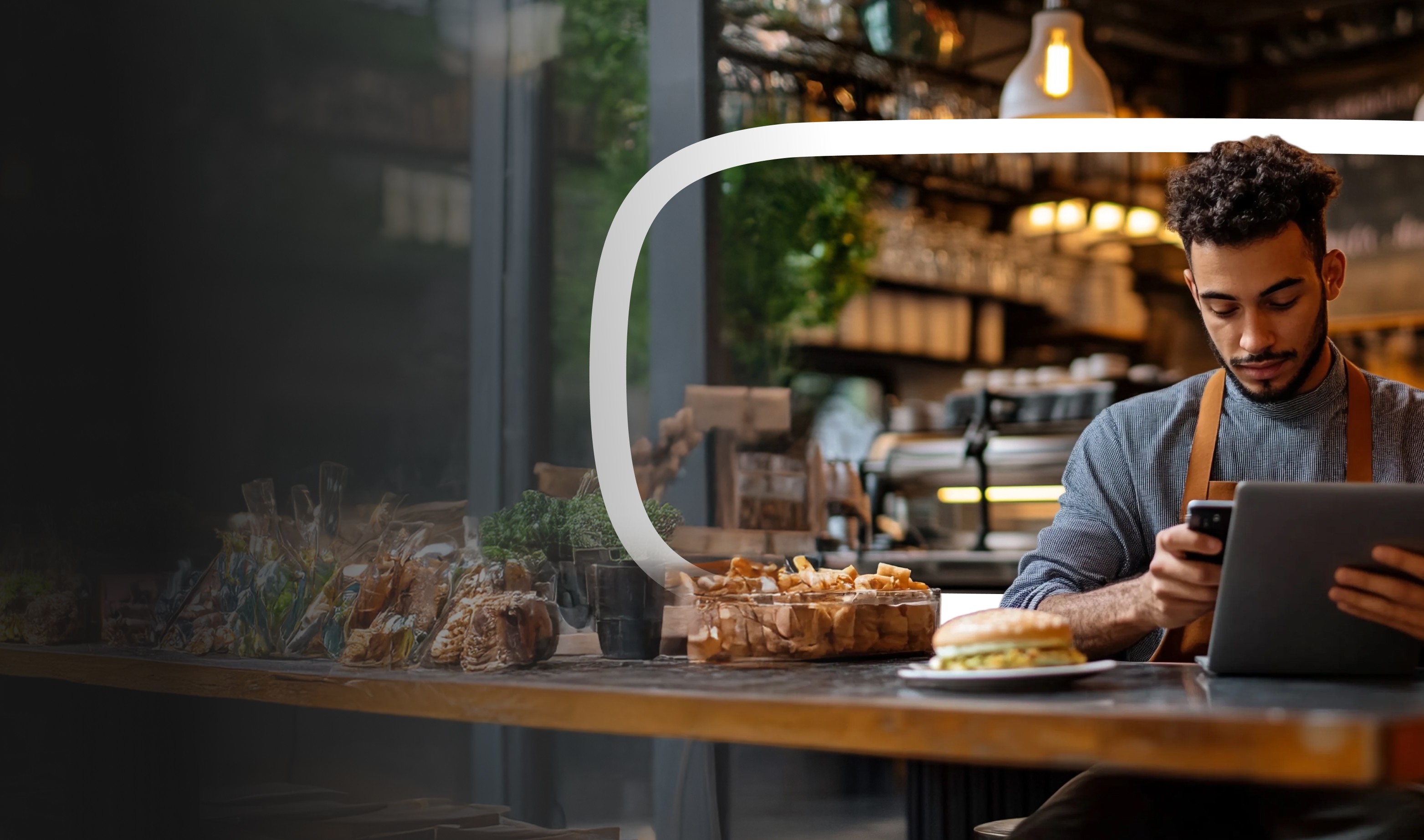 Restaurateur en tablier gérant son administratif sur smartphone et ordinateur depuis son établissement