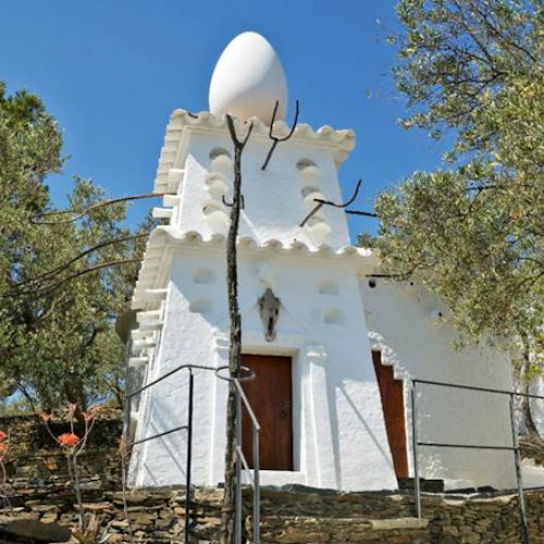 White building with an unusual egg-shaped sculpture on the roof, surrounded by trees and a clear blue sky.