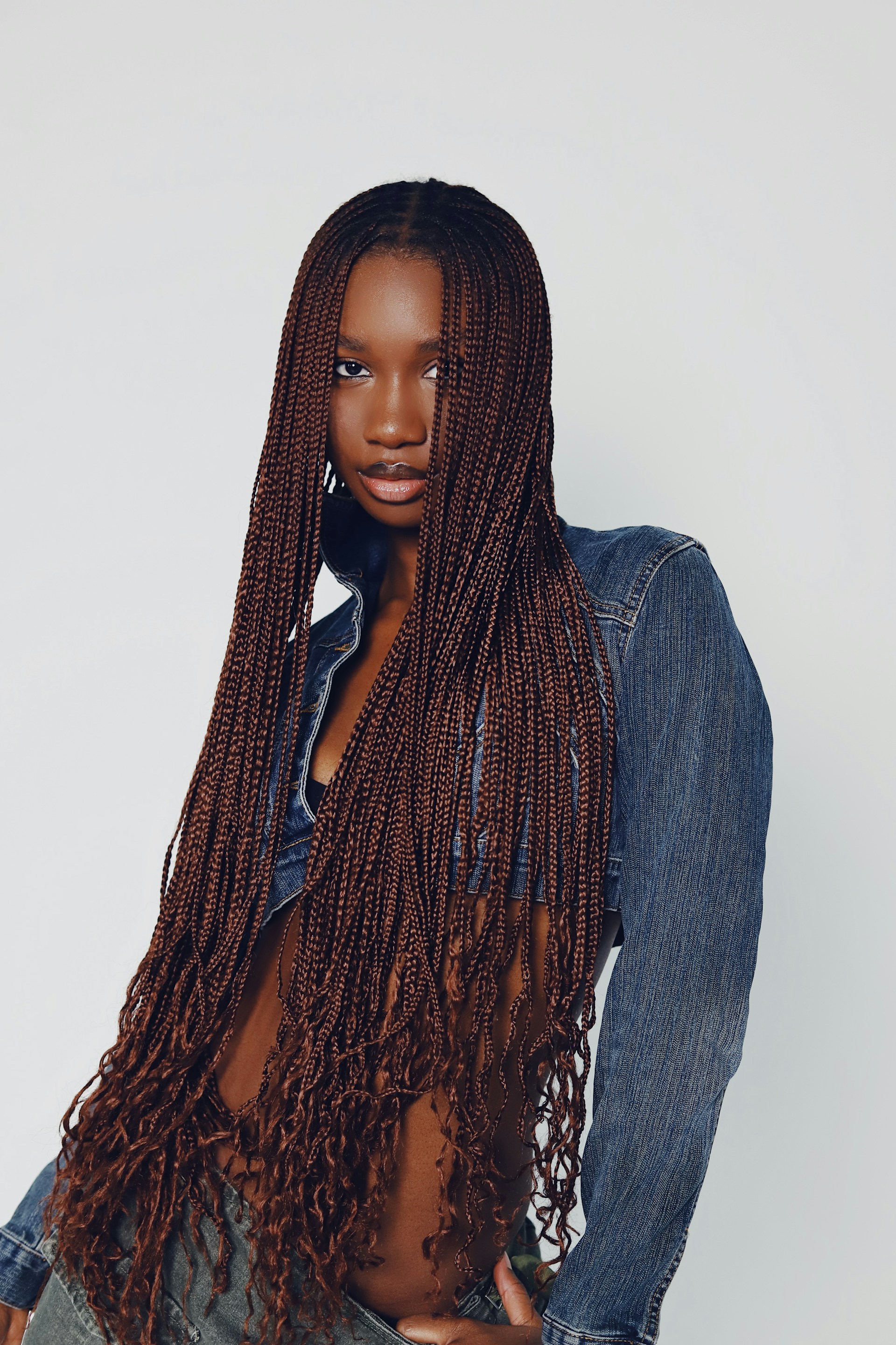 The woman with long micro-braids poses with one hand in her skirt pocket. The micro-braids reach past her waist and feature curly, unraveled ends.