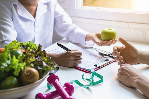 A person discusses nutrition with another, surrounded by fresh vegetables and a fitness plan on the table.