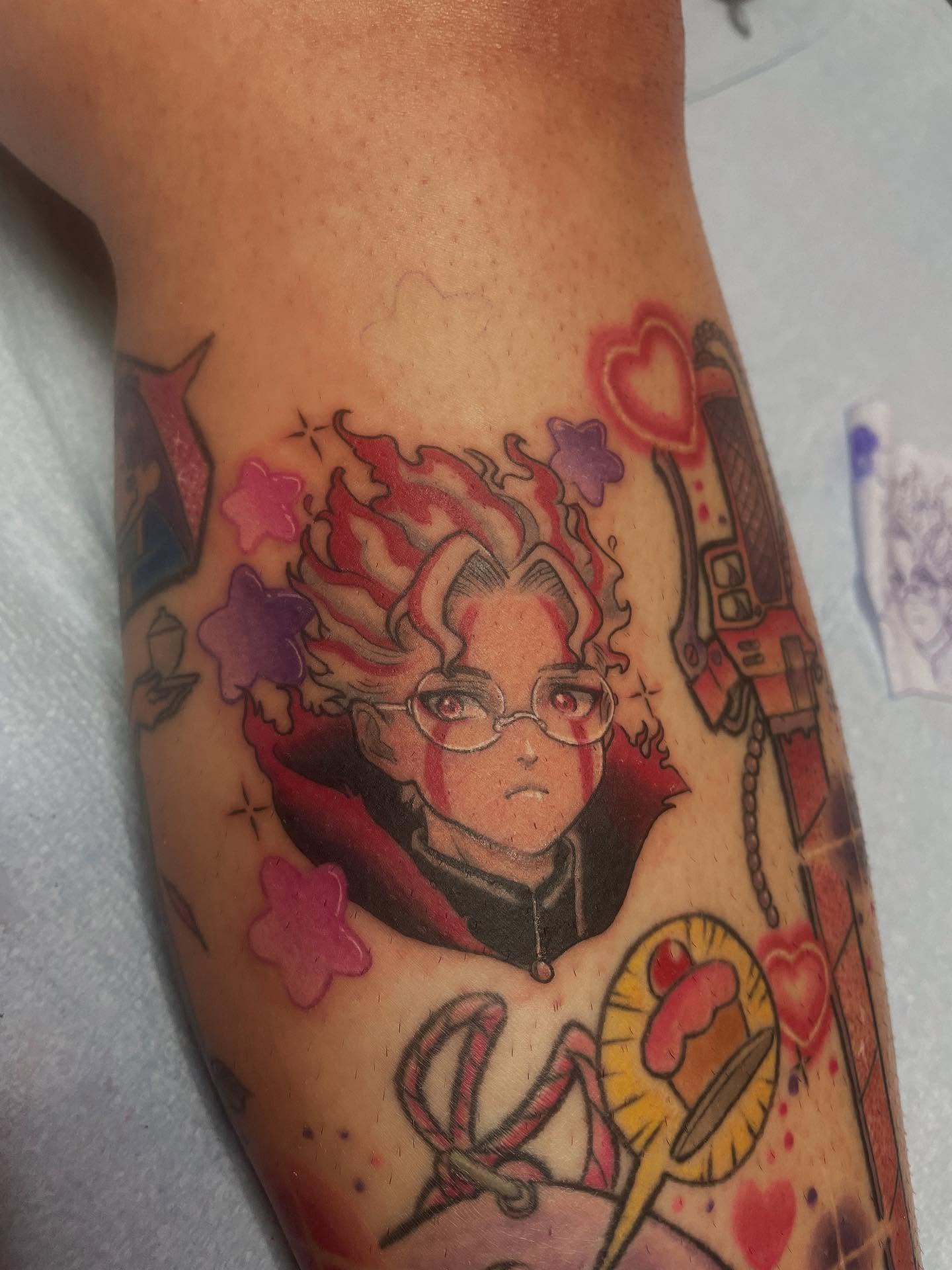 A vibrant tattoo of a chainsaw-like creature on a person's forearm. The tattoo is detailed with shades of orange, black, teal, and red.