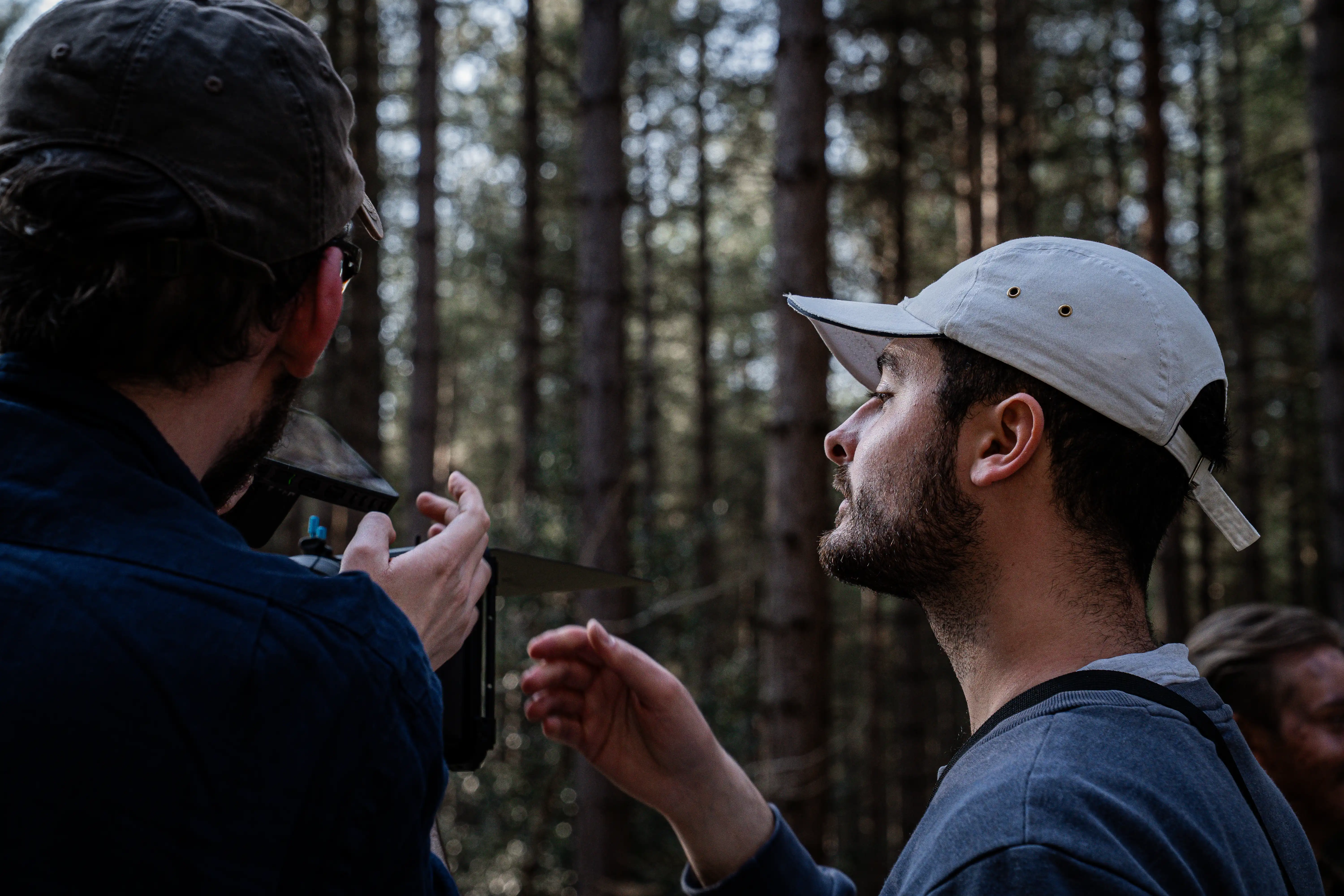 Two filmmakers operate a large camera on a dimly lit set. One wears headphones, both focused, suggesting a serious, creative atmosphere.