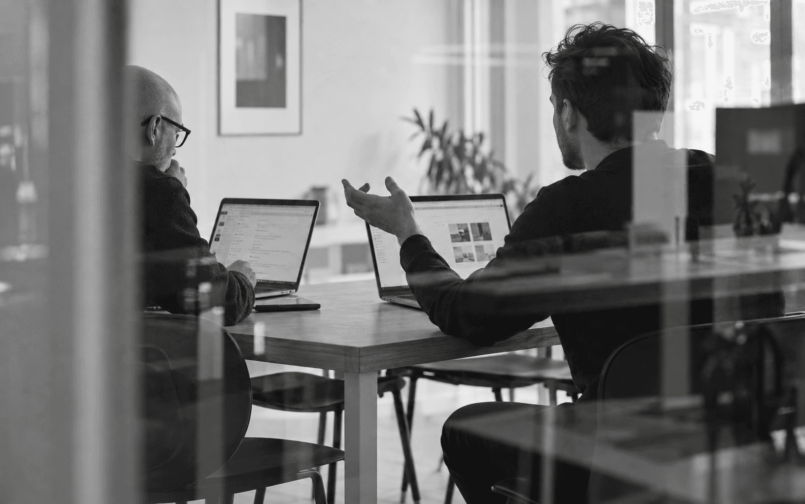 Black and white image of people working at a table with laptops, showing hands gesturing during discussion of digital content displayed on screens, with fabrica® logo in the corner.