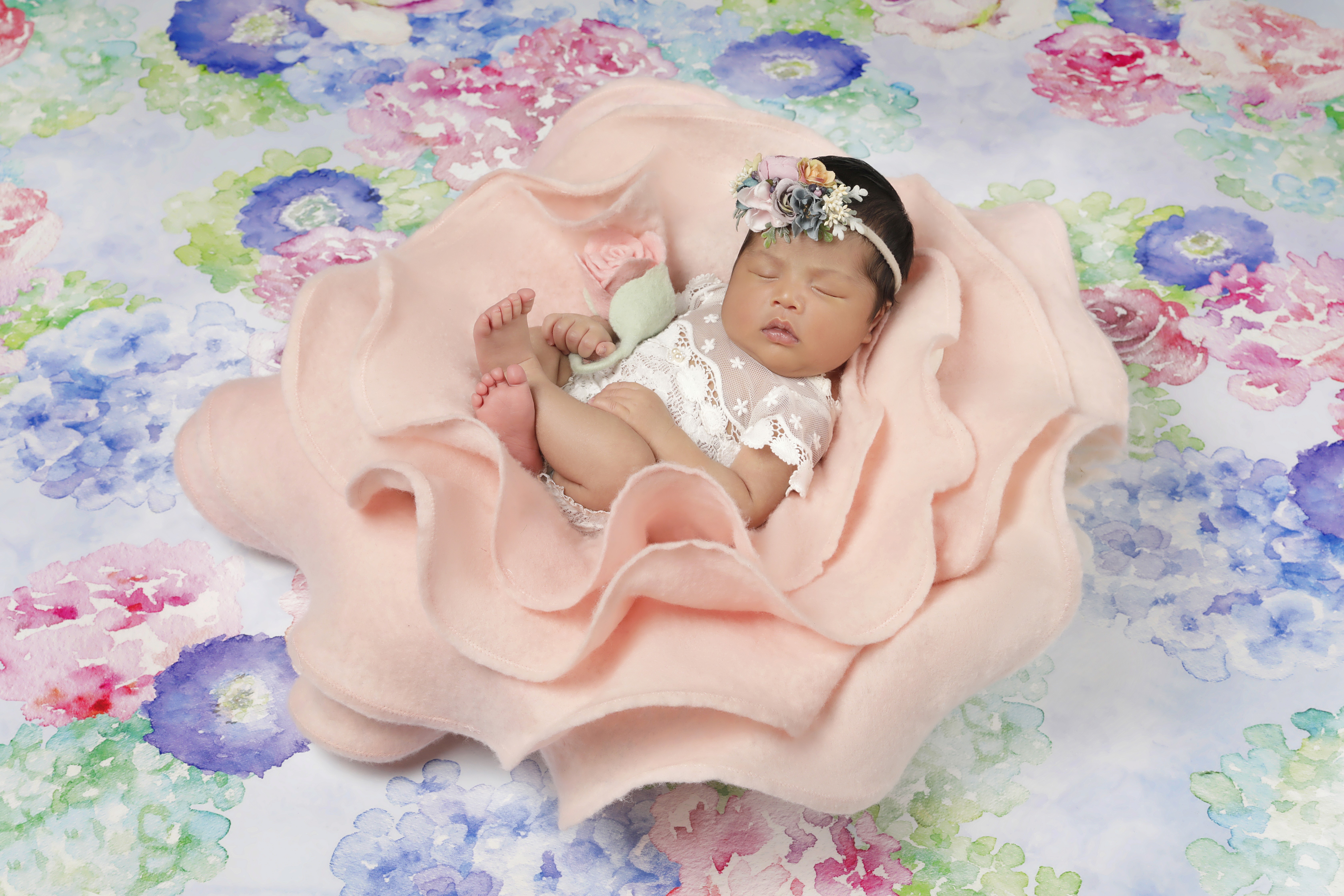A newborn baby rests peacefully in a soft pink fabric flower baby photography prop.
