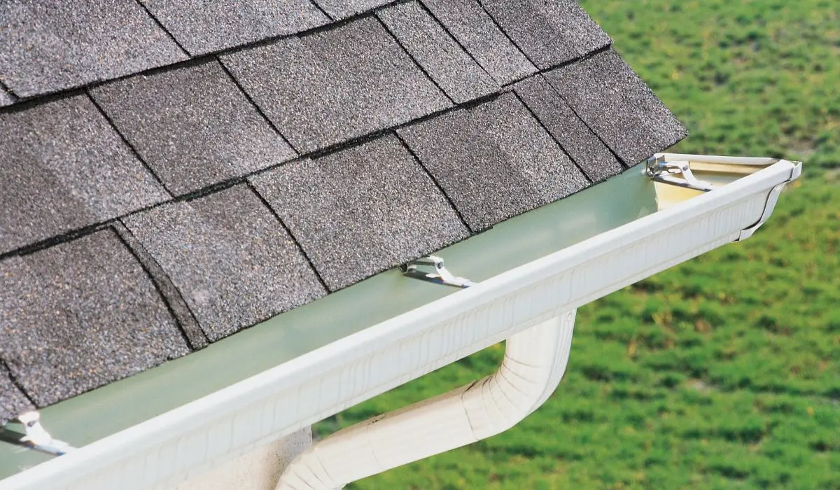 Close-up view of a newly installed white rain gutter system attached to a shingle residential roof.